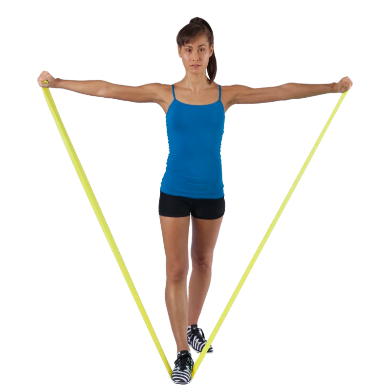 Woman exercising with Spirit Fitness Band 9 kg, latex-free, yellow resistance band, 183x10 cm, stretched under her feet and held in both hands, demonstrating fitness training use.