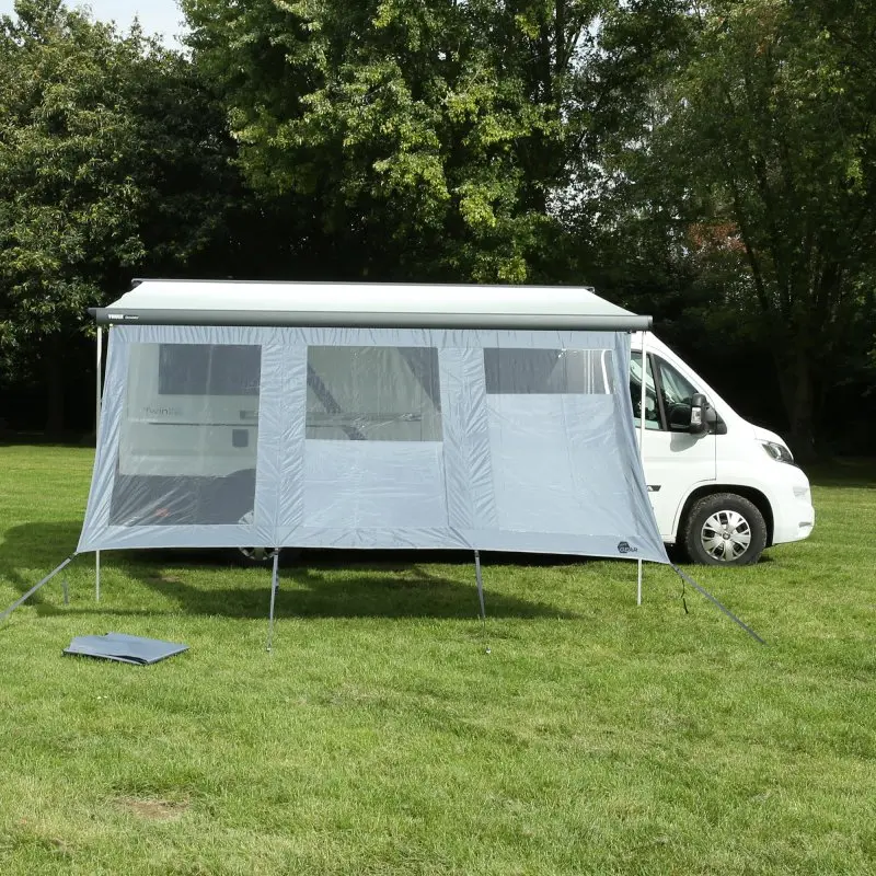 your GEAR Panorama Wall 4,3 x 2 m als Vorderwand für Markisen an Wohnmobil, schützt vor Sonne, Wind und Regen, mit großen Sichtfenstern, aufgestellt auf einer Wiese vor einem weißen Kastenwagen.