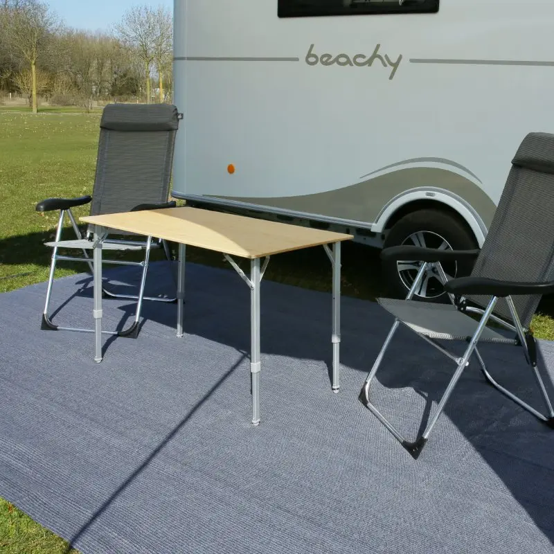 Tappeto da campeggio your GEAR Toskana 300 x 600 cm in HDPE grigio-blu, posato davanti a una roulotte, resistente alle intemperie, con tavolo e sedie da esterno sopra.