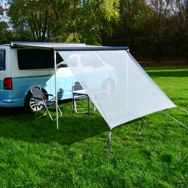 Paroi avant your GEAR Capri Sun Blocker 2,4 x 2 m montée sur un camping-car, tissu spécial transparent offrant protection solaire et intimité, installée sur une pelouse avec chaises de camping.
