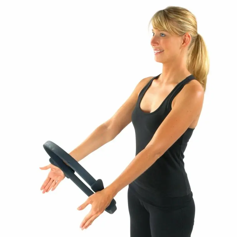 Woman in black sportswear using a Carnegie Pilates resistance ring with foam handles, demonstrating an exercise for core, arm, and shoulder training, ideal for home fitness, yoga, and Pilates workouts.