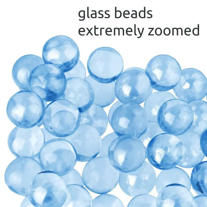 Close-up of blue glass beads, used as filling material for the yourGEAR Como 9 kg weighted therapy blanket, showing their round shape and smooth surface. Text reads "glass beads extremely zoomed".