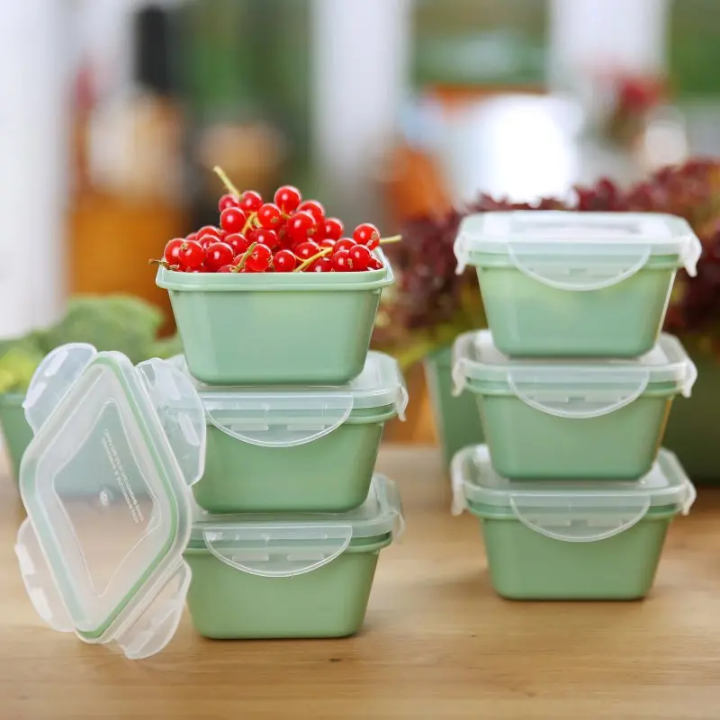 Sechs grüne your GEAR Pila Frischhaltedosen à 300 ml mit transparenten Deckeln, stapelbar auf einem Holztisch, eine Dose gefüllt mit roten Johannisbeeren, ideal zur Lebensmittelaufbewahrung.