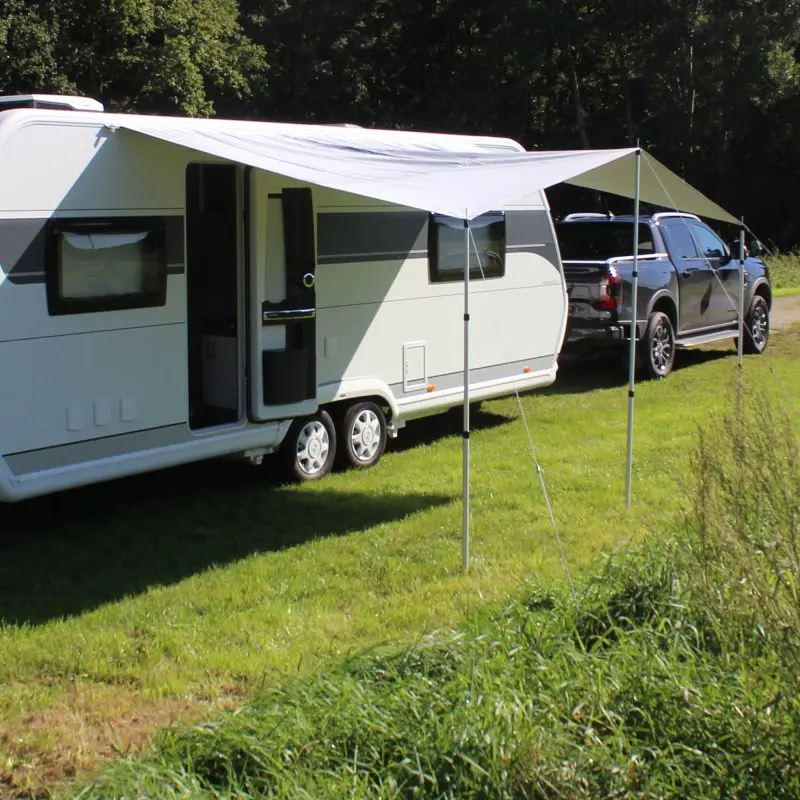 your GEAR Caravan Thermo Tarp 435 x 250 cm, UV80 sun canopy with reflective aluminum coating, mounted on a caravan, provides opaque, waterproof, and insulated shade on a grassy campsite.