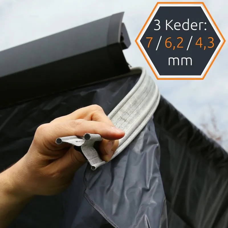 Main tenant une bande d'étanchéité grise à triple keder pour paroi de store, joint textile renforcé fixé à une toile grise foncée, compatible markises 240x200 cm your GEAR Korsika, gros plan détail insert keder.