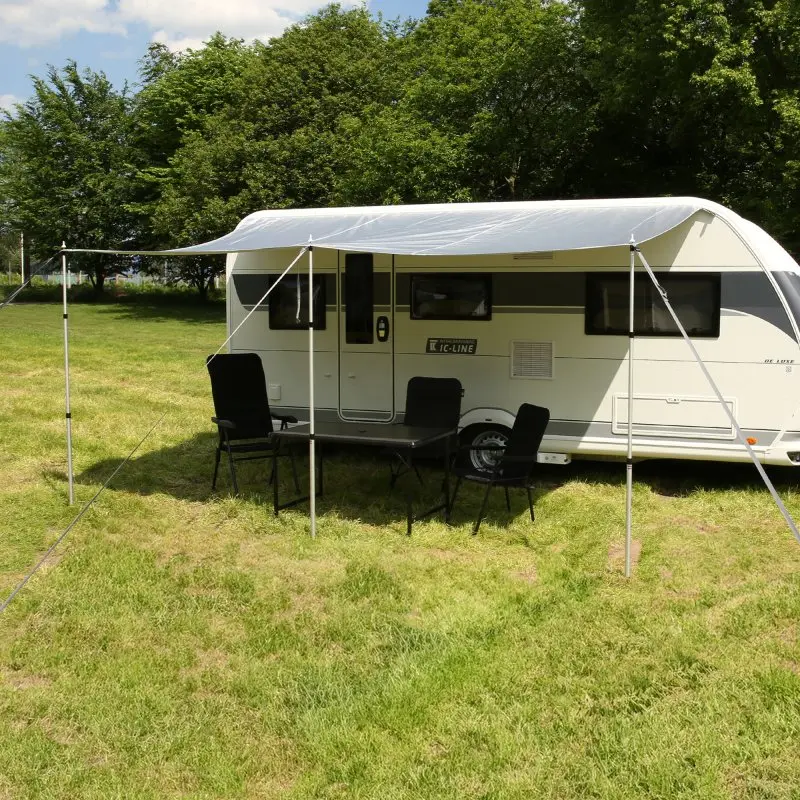 Caravan Thermo Tarp 435 x 250 cm by your GEAR, UV80+, waterproof, opaque, with reflective aluminum coating, mounted as a sun canopy on a caravan with outdoor chairs and table underneath.