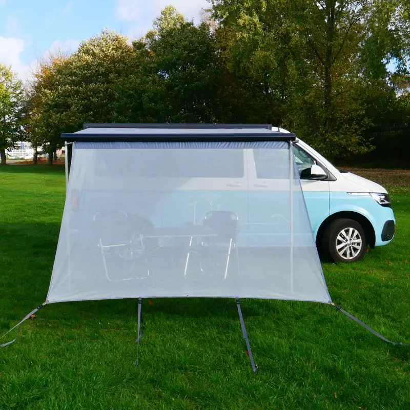 Paroi avant your GEAR Capri Sun Blocker 2,4 x 2 m montée sur une marquise de camping-car, tissu transparent protégeant du soleil, fixée au sol, camping-car bleu en arrière-plan sur pelouse verte.