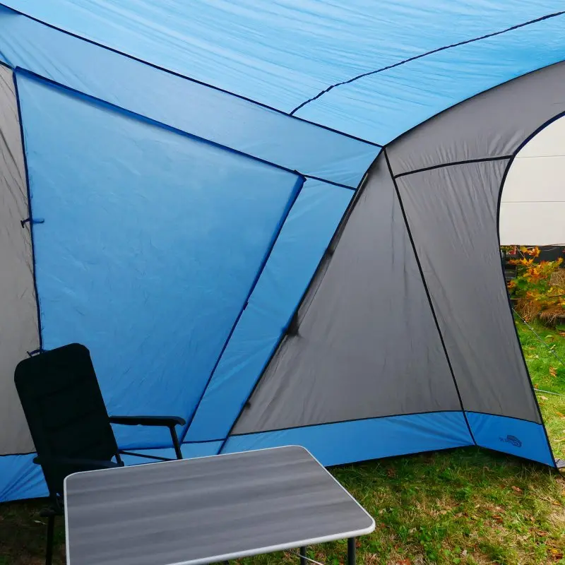 Blau-graues your GEAR Sharki 330 Wohnwagen Sonnendach mit Alugestänge, zwei großen Seitenfenstern, Campingstuhl und Tisch auf Rasen, ideal als Vorzelt oder Sonnenvordach für Kurzurlaube.