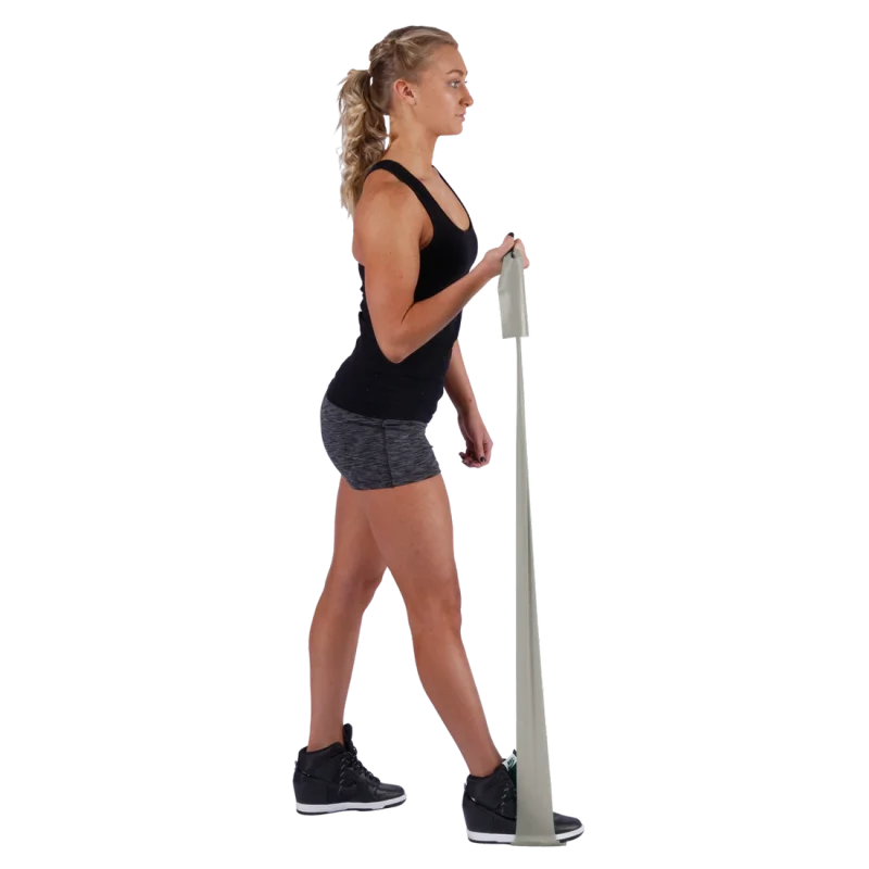 Woman exercising with Spirit Fitnessband, 183x10 cm, latex-free, 22.5 kg resistance. The grey resistance band is stretched from foot to hand, suitable for strength and rehabilitation training.