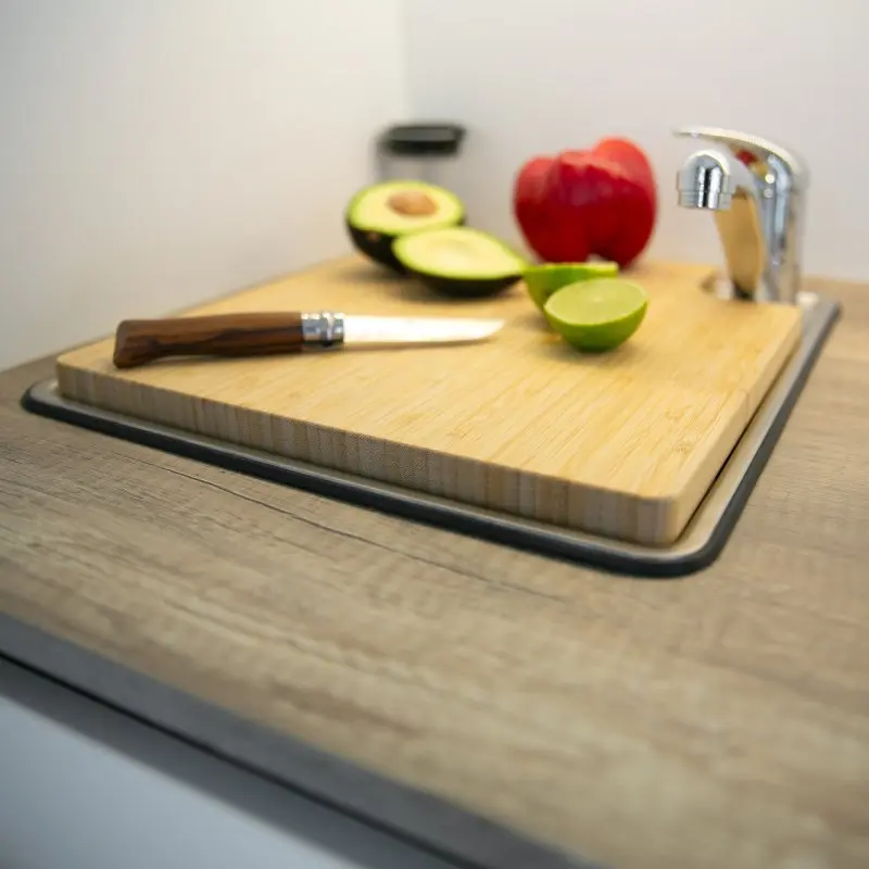 your GEAR Burano Bambus Spülbeckenabdeckung und Schneidebrett, passgenau auf einem Wohnwagen-Spülbecken platziert, mit Messer, Avocado, Limette und Paprika, ideal als Caravan Küchenzubehör.