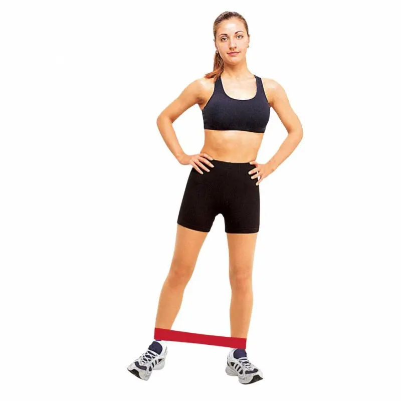 Woman demonstrating a red Carnegie latex fitness resistance band looped around her legs, wearing black sportswear. Ideal for strength training, rehabilitation, and versatile workouts. Band size: 52x5 cm.