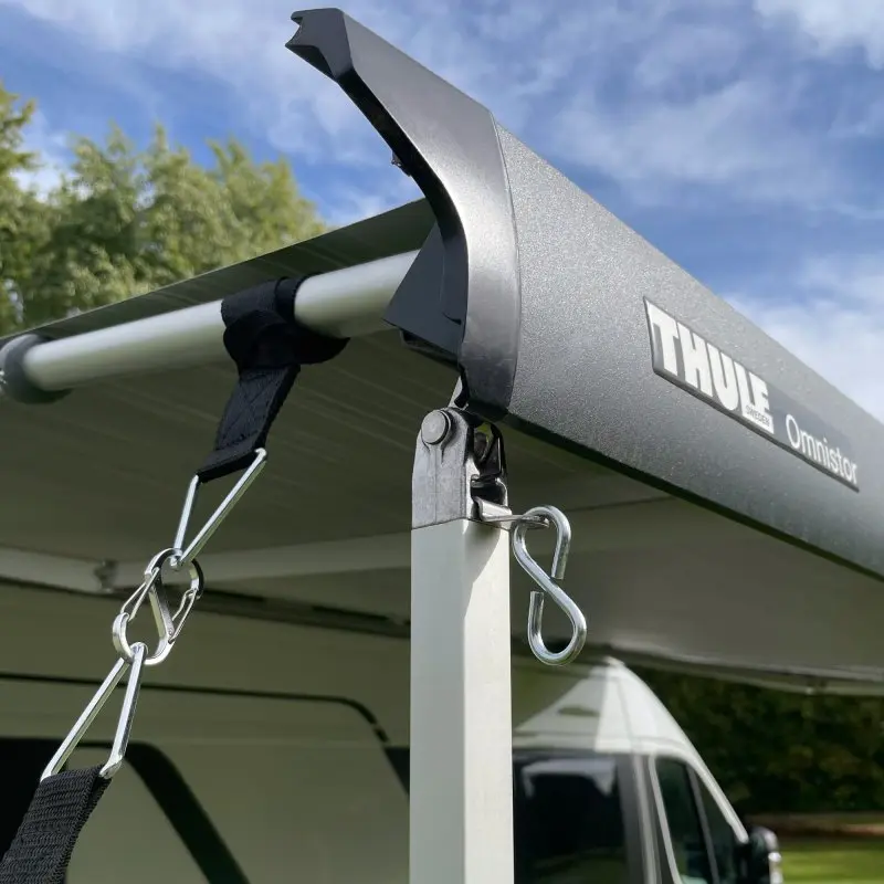 Markisen-Sturmsicherungsset von your GEAR an einer ausgefahrenen Markise montiert, mit robusten Spanngurten, Karabinern und Haken zur sicheren Befestigung am Caravan bei sonnigem Wetter.